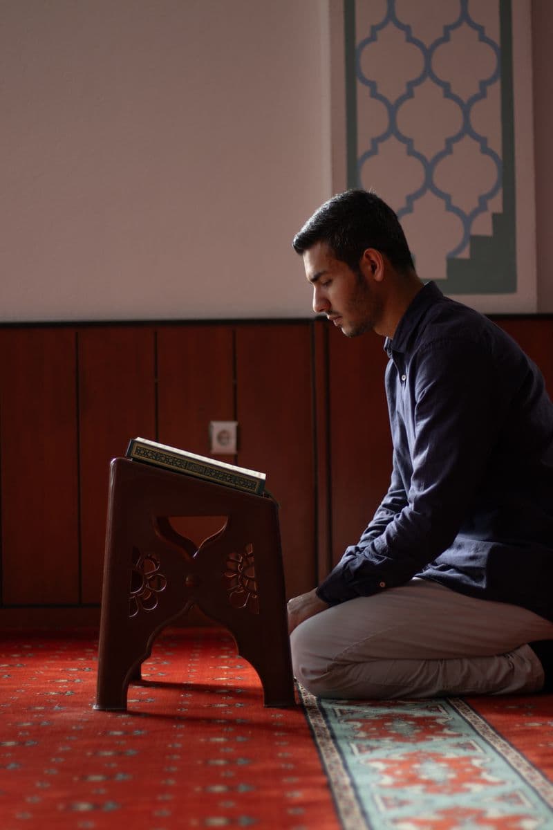 A man engaged in prayer inside a mosque, beside a Quran