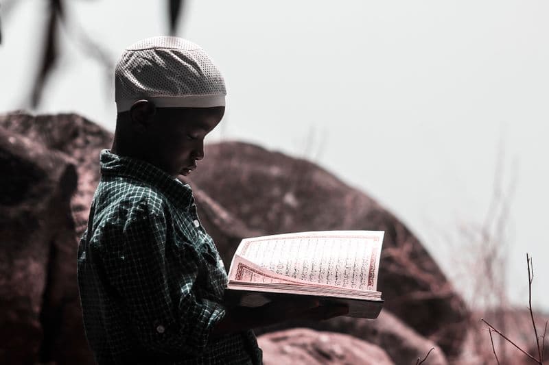A young girl in a hijab reciting the Quran indoors